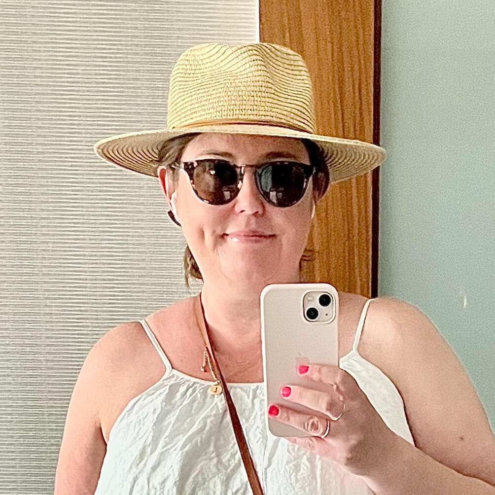 Lauren Photo of a middle aged white woman with sunglasses and brown hair in a bun. She is smiling at the camera and is taking a selfie of her head and shoulders in a mirror.